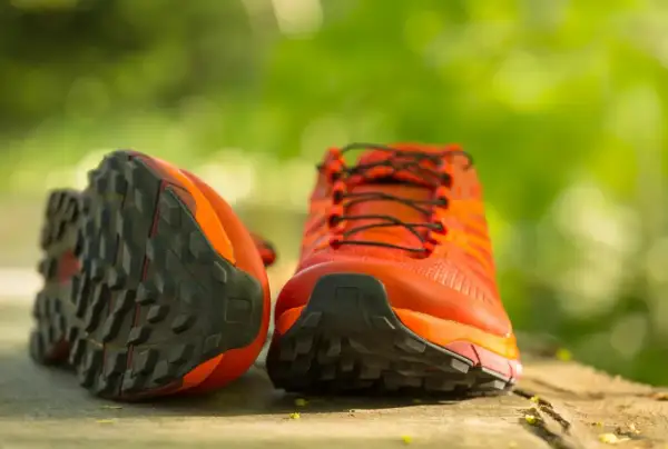 Leuchtend orange Wanderschuhe mit grobstolliger Sohle, bereit, neu besohlt zu werden für neue Abenteuer.
