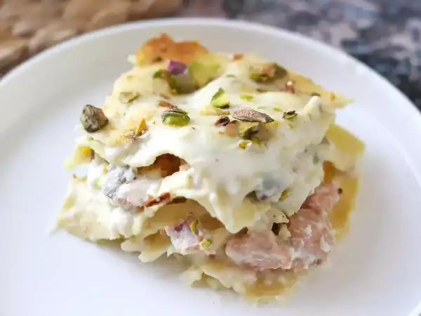 Porzione di lasagne bianche sfiziose con pistacchi e un ripieno cremoso, servite su un piatto bianco.