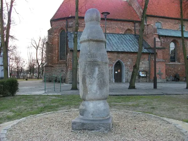 Kamienny słup milowy z inskrypcją przed ceglanym kościołem.