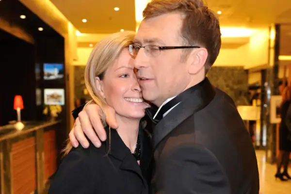 Maciej Orłoś z żoną, uśmiechnięci, w eleganckich strojach, w intymnym uścisku.