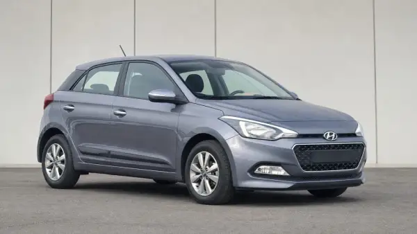 Szary Hyundai i20 z włączonymi światłami pozycyjnymi na tle jasnej ściany.