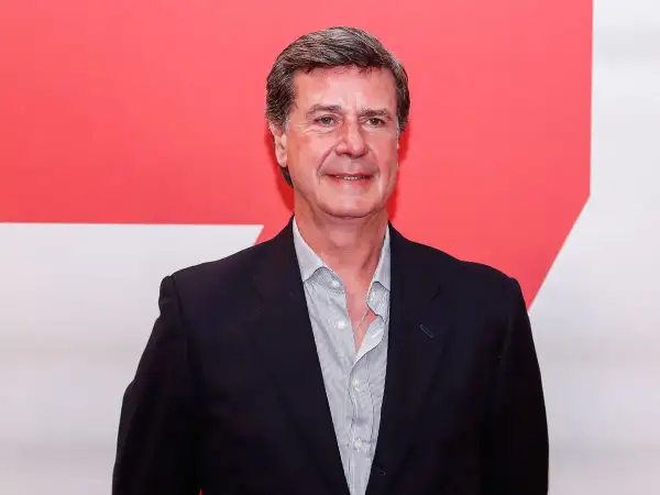Javier Martínez de Irujo, con traje oscuro y camisa a rayas, sonríe ante un fondo rojo y blanco.