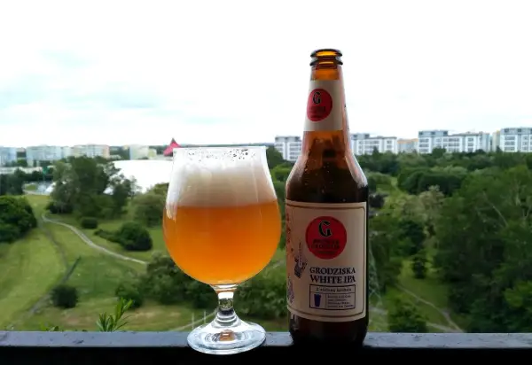 Grodziska White IPA w szkle i butelce, z widokiem na zielone miasto. Idealne na letni wieczór.