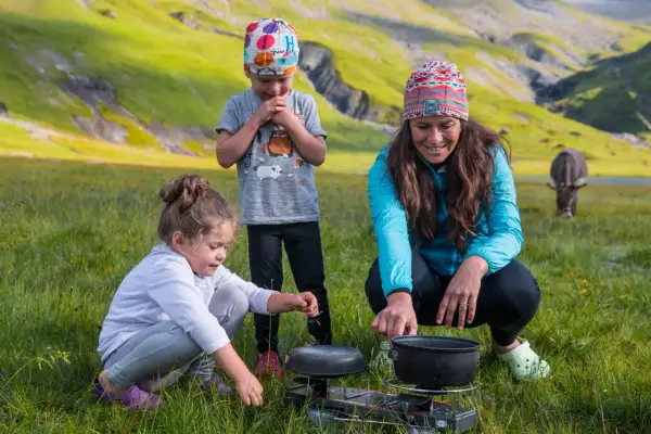 Une famille profite d'une micro aventure en famille dans un paysage montagneux verdoyant, préparant un repas en plein air.