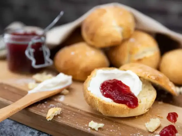 Lyxiga scones med grädde och sylt på en träbricka. En härlig fika!