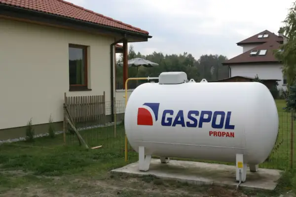 Biały zbiornik na gaz propan z logo GASPOL obok domu, zapewniający ogrzewanie gazem LPG.