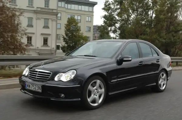 Czarny Mercedes W203 w ruchu, świeci się jedna żarówka mijania, sugerując potrzebę wymiany.