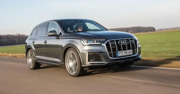 Szary Audi Q7 z napędem quattro pędzi po drodze, mijając zielone pola.