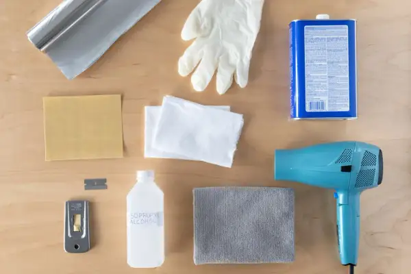 Kit pour savoir comment enlever du double face sur du carrelage : sèche-cheveux, grattoir, alcool isopropylique, gants, chiffons, papier de verre et rouleau d'aluminium.