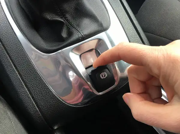Dito, un dito preme il pulsante del freno a mano elettronico, simbolo di sicurezza e modernità.