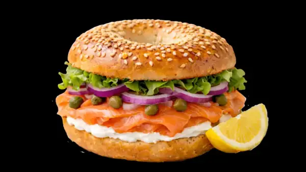 Un délicieux bagel saumon garni de fromage frais, oignons rouges, câpres et laitue, avec un quartier de citron à côté.