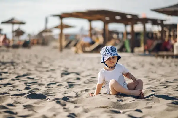 Uroczy maluch w kapelusiku na plaży. Idealne miejsce, gdzie na wakacje z rocznym dzieckiem.