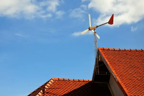 Małe wiatraki energetyczne na dachu domu, obracające się na tle błękitnego nieba z chmurami.
