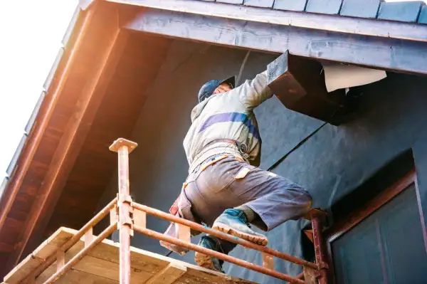 Un ouvrier en pose isolation extérieur sur un chantier, travaillant sur un bardage en bois.