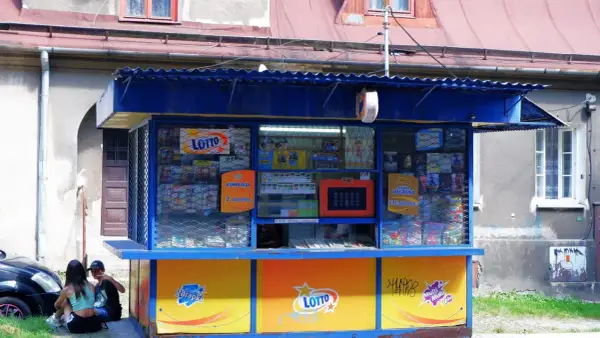 Kiosk Lotto z ekspozycją zdrapek i informacją o kumulacji. Dzieci siedzą obok, zastanawiając się, dlaczego kolektorzy nie chcą sprzedawać zdrapek z konkretnych numerów paczek.