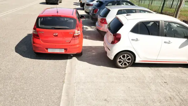Coches aparcados en batería, un rojo y un blanco, junto a una acera.