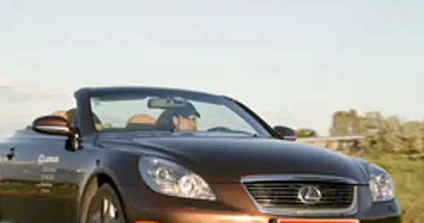 Brązowy kabriolet Lexus SC430 z otwartym dachem, kierowca w czapce, jazda w słoneczny dzień.