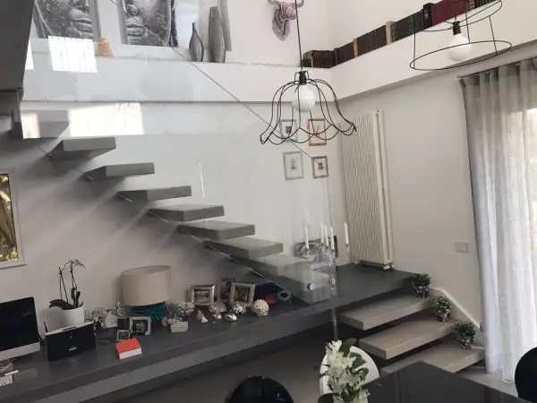 Scala interna moderna con gradini a sbalzo e parapetto in vetro. Un modo elegante per come abbellire una scala interna con decorazioni e piante.