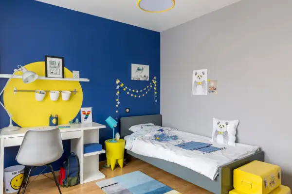Cameretta con parete blu vivace e decorazioni a stelle. Scrivania bianca, letto grigio, cuscino panda. Ottime idee pittura cameretta per un ambiente allegro.