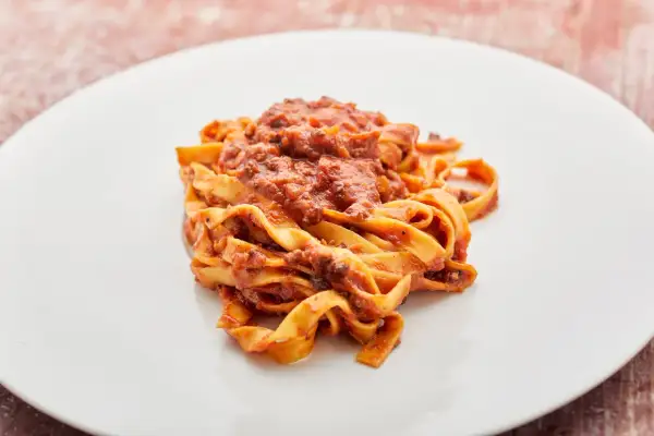 Breite Bandnudeln mit einer herzhaften vegetarischen Bolognese-Sauce auf einem weißen Teller.