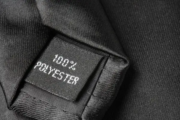Czarna metka z napisem "100% POLYESTER" na tle eleganckiej tkaniny. Czy poliester się rozciąga? Ten materiał wygląda na wytrzymały.