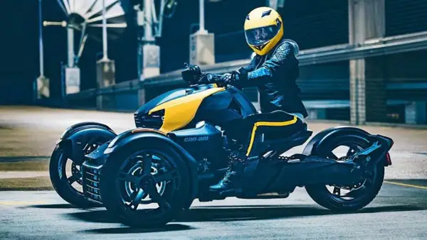 Kierowca w żółtym kasku na futurystycznym motorze trójkołowym Can-Am, gotowy do jazdy.