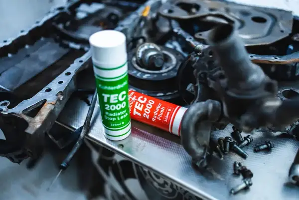 Uszkodzony cylinder objawy? Na stole leżą części silnika i dwa preparaty TEC 2000: Radiator Stop Leak i Radiator Flush.