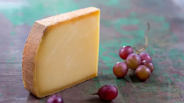 Un morceau de Comté aux cristaux savoureux, accompagné de grappes de raisins rouges sur un fond texturé.