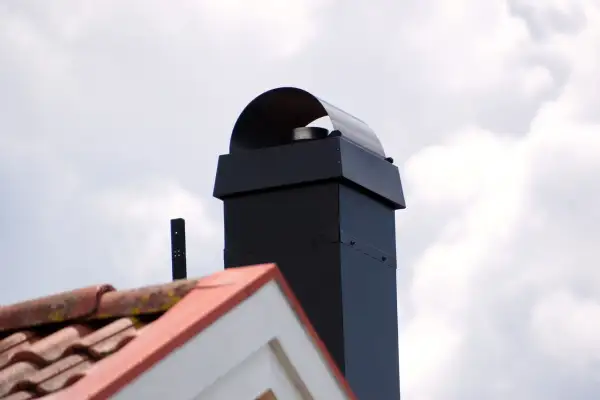 Schwarzer Schornstein mit Haube, Dachziegel und ein kleines schwarzes Rohr. Beachten Sie die schornstein revisionsklappe vorschriften.