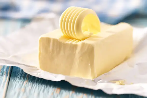 Un rouleau de beurre jaune, frais et crémeux, est posé sur un bloc de beurre, prêt à être tartiné.