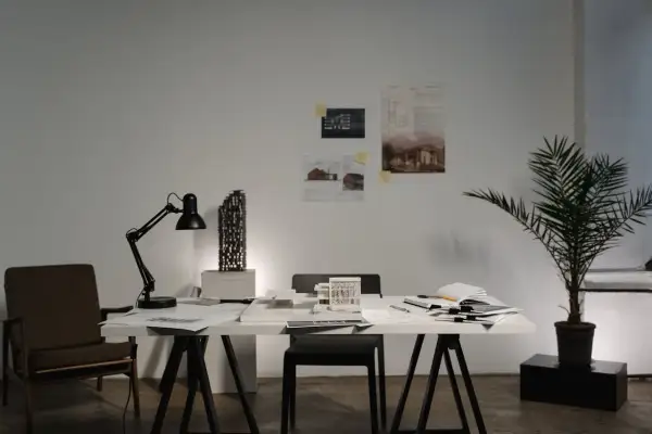 Biuro architektoniczne z modelem budynku, lampą, krzesłem i dokumentacją. Karta nadzoru autorskiego czeka na zatwierdzenie.