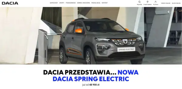 Szara dacia elektryczna Spring Electric z pomarańczowymi akcentami ładuje się przy stacji.