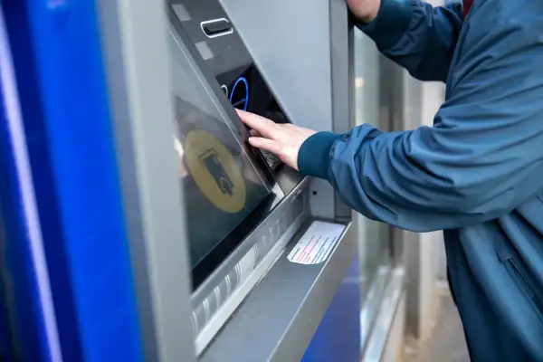 Osoba w granatowej kurtce korzysta z bankomatu, by dokonać żabka wypłata gotówki.
