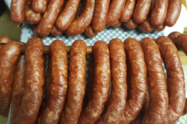 Prawdziwa wiejska kiełbasa przepis: świeżo uwędzone, rumiane kiełbaski wiszą na drewnianych kijach, gotowe do spożycia.