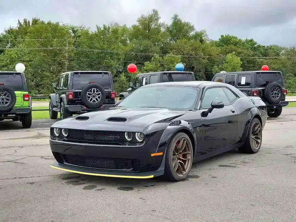Czarny Dodge Challenger SRT z żółtym akcentem na zderzaku. Obok inne samochody i balony. Sprawdź dodge challenger cena!