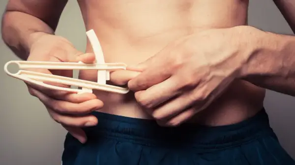 Uomo con plicometro misura il grasso corporeo, un dettaglio per capire il significato di ectomorfo e la sua costituzione fisica.