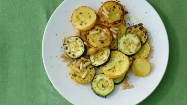 Zucchini gebraten italienisch mit Pinienkernen auf einem weißen Teller. Ein köstliches Gericht, das an einen sonnigen Tag in Italien erinnert.