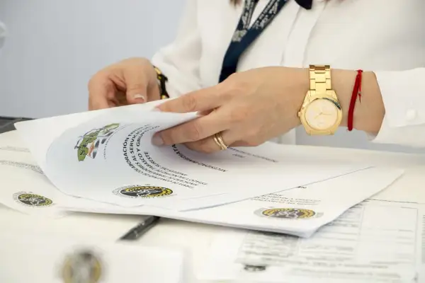 Dłonie przeglądają dokumenty, wśród których znajdują się oświadczenia o poddaniu się egzekucji. Złoty zegarek i czerwona nitka na nadgarstku.