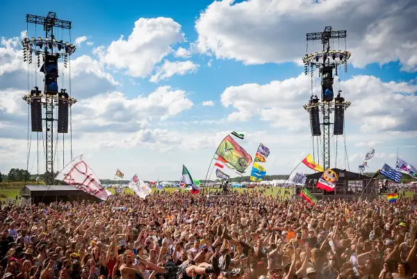 Tłum ludzi na festiwalu pod sceną z wieżami nagłośnieniowymi i flagami.