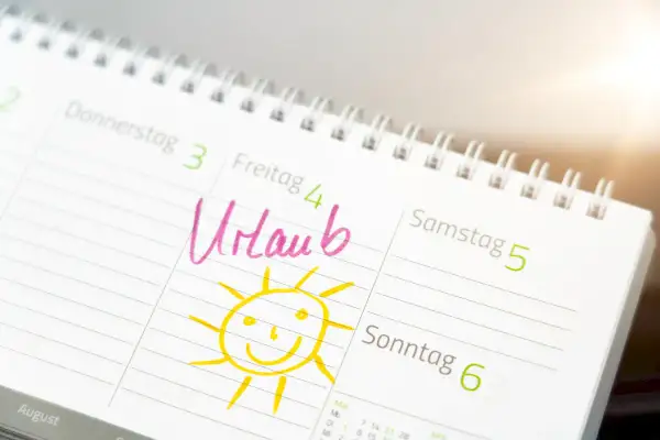 Kalendarz z zaznaczonym "Urlaub" (urlop) i uśmiechniętym słońcem. Dzień wolny w Niemczech, czas na odpoczynek!