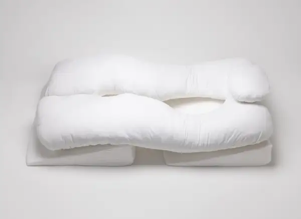 A white, U-shaped body pillow, designed for comfort and support, rests on wedge-shaped cushions. These almohadas ortopédicas offer a cozy embrace.