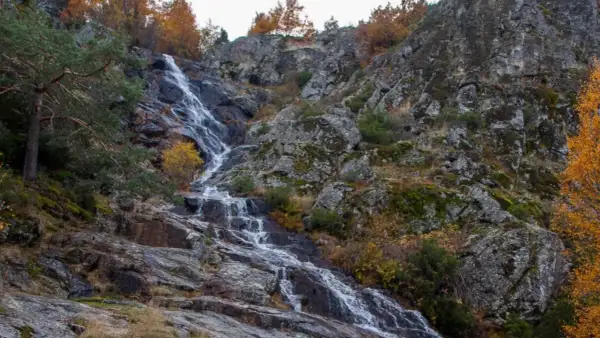 Cascada de Mojonavalle en otoño, con rocas cubiertas de musgo y árboles de hojas doradas.