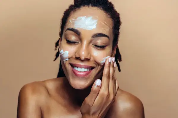 Une femme applique une crème hydratante sur son visage, un geste essentiel pour un maquillage jour parfait.