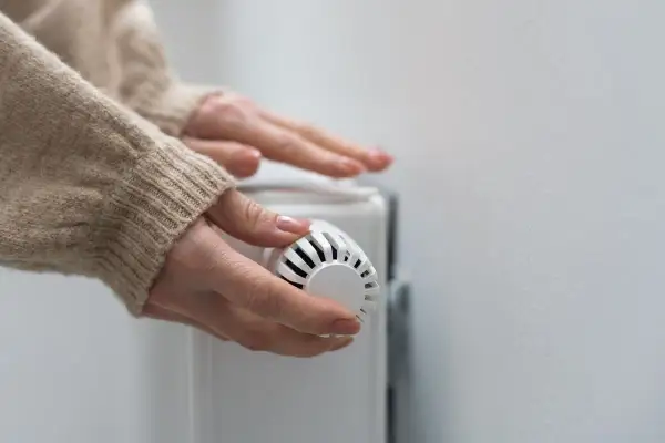 Mains mains sur un radiateur, ajustant le thermostat pour contrôler le prix du chauffage au gaz.