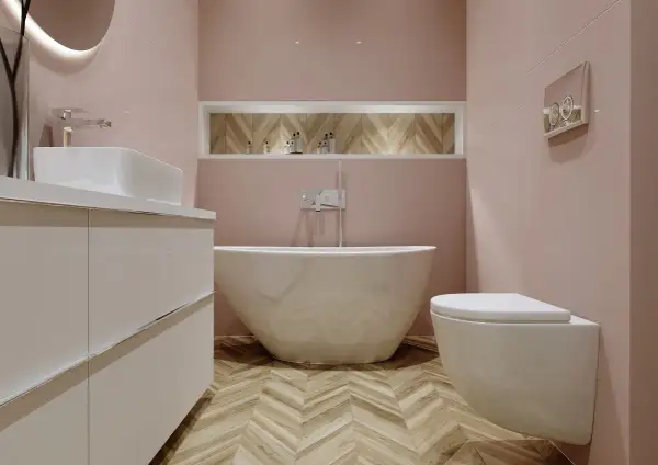 Elegancka łazienka z wolnostojącą wanną i baterią wannową. Jasnoróżowe ściany, drewniana podłoga w jodełkę.