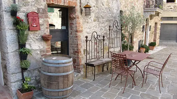 Un angolo pittoresco nella regione del Chianti con un barile di legno, piante aromatiche, un tavolino da esterno e un vecchio cancello in ferro battuto.