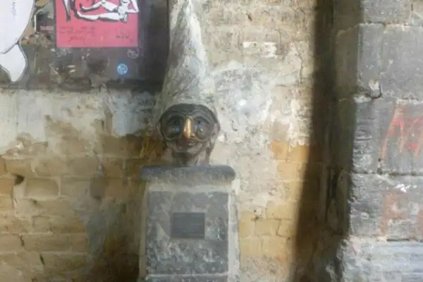 Busto con cappello a cono e un buffo naso di Pulcinella, su un piedistallo di pietra.
