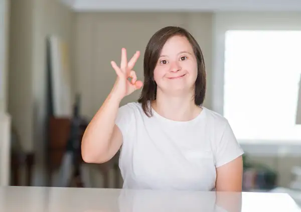 Ragazza con sindrome di down sorride e fa il segno "ok" con la mano.