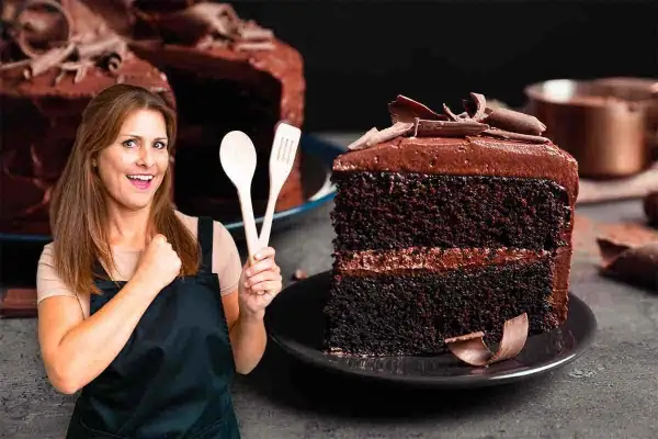 Donna sorridente con mestoli in mano, accanto a una fetta di torta tenerina Bimby, ricca e golosa.