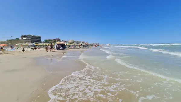 Spiaggia affollata a Senigallia mare, con ombrelloni, lettini, bancarelle e gente che passeggia. Il mare azzurro e calmo invita a un tuffo.